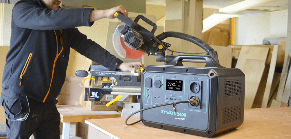 Batterie IZYWATT qui est alimente une disqueuse dans un atelier et la disqueuse est en fonctionnement et semble couper du bois, atelier, charpentier