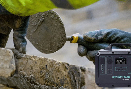 Maçon qui construit un mur à l'aide de sa truelle, ciment, brique et Batterie IZYWATT 2 400