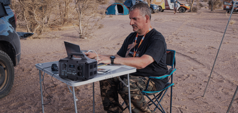 Homme assis, Batterie IZYWATT qui charge un ordinateur portable, équipement de camping, radio,